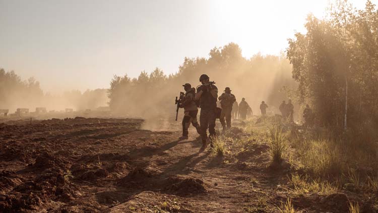 A group of soldiers goes through the field along the forest in t