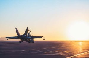 Jet fighter on an aircraft carrier deck against beautiful sunset sky .