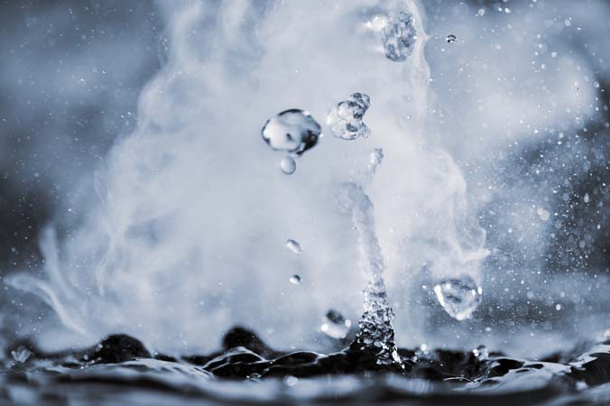 Boiling water splash with steam on black background closeup